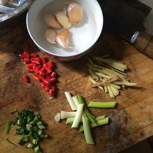一位厨师正在木质砧板上用刀切碎几根红色的小米椒,旁边放着蒜末和青葱,光线柔和,突出食材的新鲜感和烹饪氛围 厨房中切碎小米椒的场景