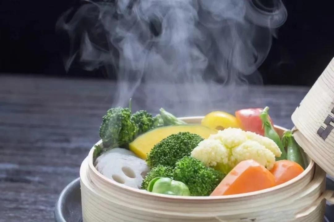 一位家庭主妇在现代化厨房中使用竹蒸笼蒸制新鲜白色的菜花,锅中有蒸汽上升,旁边放着绿色香草和柠檬片,展现健康烹饪方式 家庭厨房中正在蒸制新鲜菜花的场景