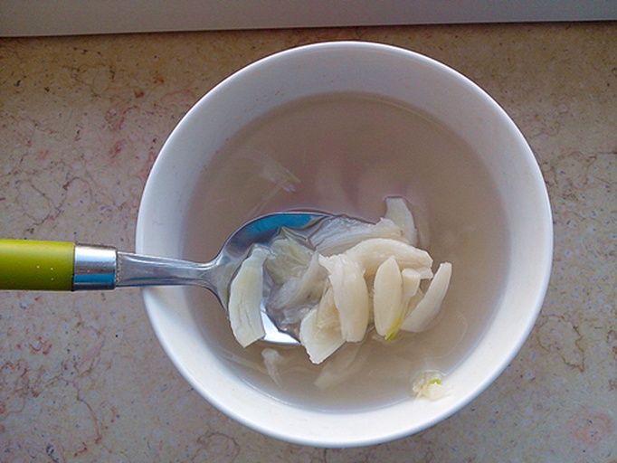一碗盛满乳白色骨头汤的瓷碗,汤面漂浮着油花和葱花,背景可见炖煮用的砂锅和剩余的白芷药材片 成品白芷骨头汤特写