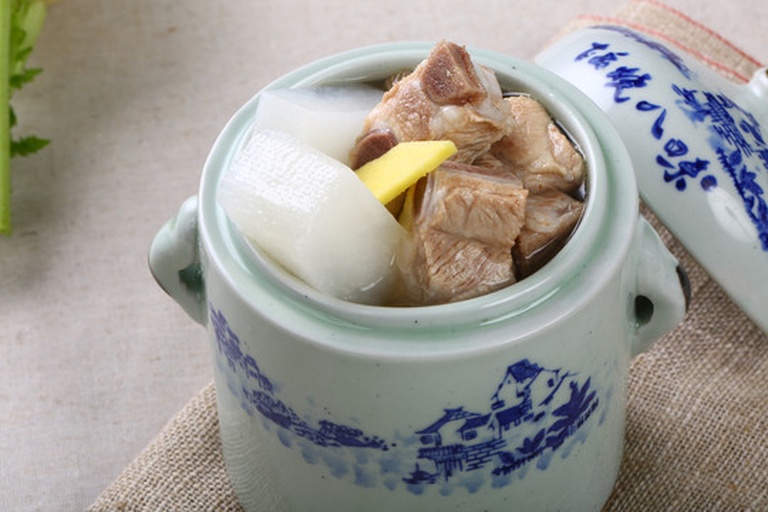 不锈钢汤锅中炖煮着青萝卜与排骨,汤面漂浮少许油花,旁边放置一根完整的青萝卜用于尺寸对照,展示从原料到成品的转化过程 一锅正在炖煮的青萝卜排骨汤,汤色清澈微白,青萝卜块清晰可见,锅边摆放整根未处理的青萝卜作为对比