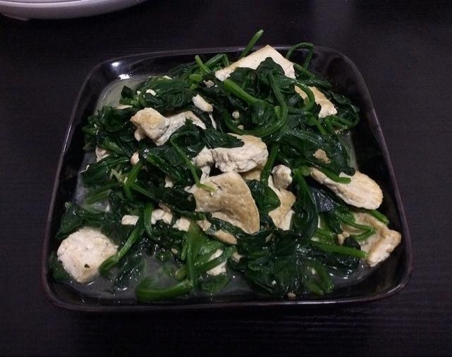一盘刚出锅的清炒菠菜千叶豆腐,翠绿的菠菜与乳白的豆腐交织,表面有轻微油光,撒有少许蒜末,盛放在白色瓷盘中,背景虚化体现家庭餐桌氛围 清炒菠菜千叶豆腐成品图
