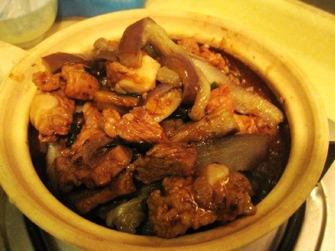 一口深色砂锅正在慢火炖煮土豆炖茄子,锅内食材翻滚,茄子与土豆已部分融合,汤汁浓稠,蒸汽升腾,旁边摆放着酱油瓶和调料罐,展现真实厨房场景 土豆炖茄子炖煮过程