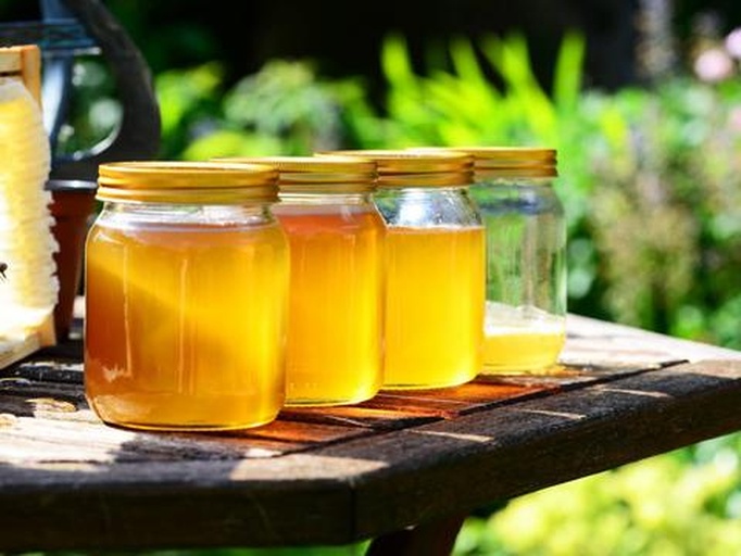 一位女性在厨房水槽前用清水冲洗几颗金黄色的金桔,旁边放着玻璃杯和蜂蜜罐,窗外透进自然光,营造出健康生活的温馨氛围 家庭主妇正在清洗金桔准备泡水