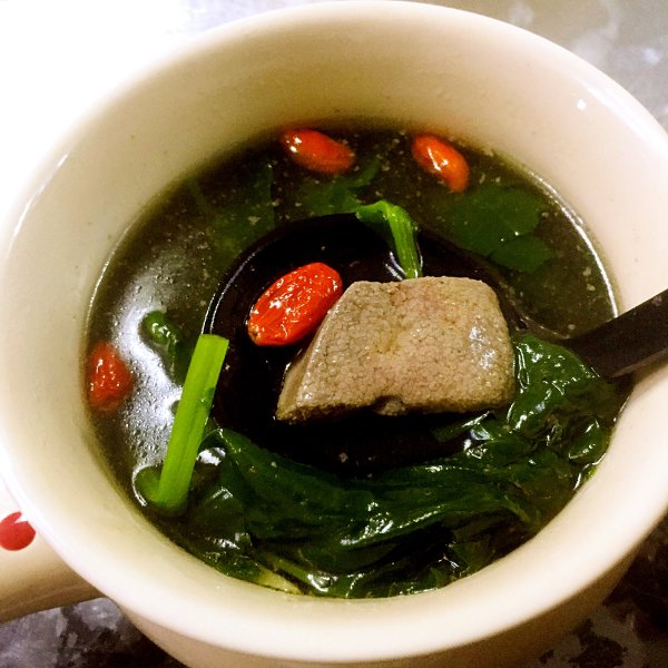 菠菜熬猪肝汤特写：翠绿菠菜叶与深褐色猪肝片在清亮琥珀色汤中自然分布，汤面浮有细微油星，无添加调味料痕迹，体现原生态烹饪