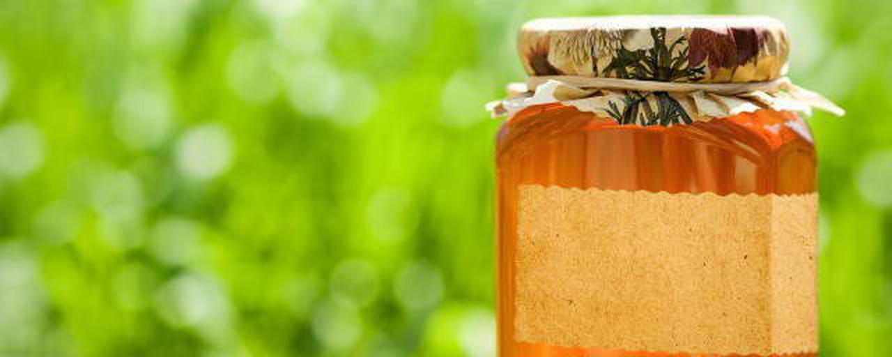 一瓶透明玻璃罐装的天然蜂蜜,清晰可见上层为清亮液体,下层为白色絮状或颗粒状沉淀,背景为木质餐桌和蜜蜂采蜜插画,光线柔和,突出自然健康主题 蜂蜜分层示意图