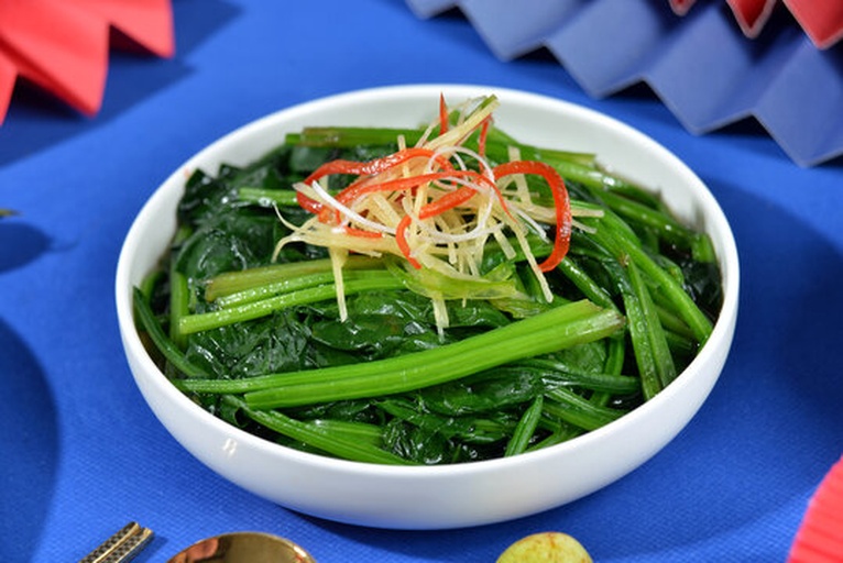 一盘刚出锅的姜丝炒菠菜,金黄色的姜丝与翠绿的菠菜交织,表面略带油光,盛放在白色瓷盘中,背景为家庭厨房灶台,体现家常健康烹饪场景 家常小炒:姜丝炒菠菜