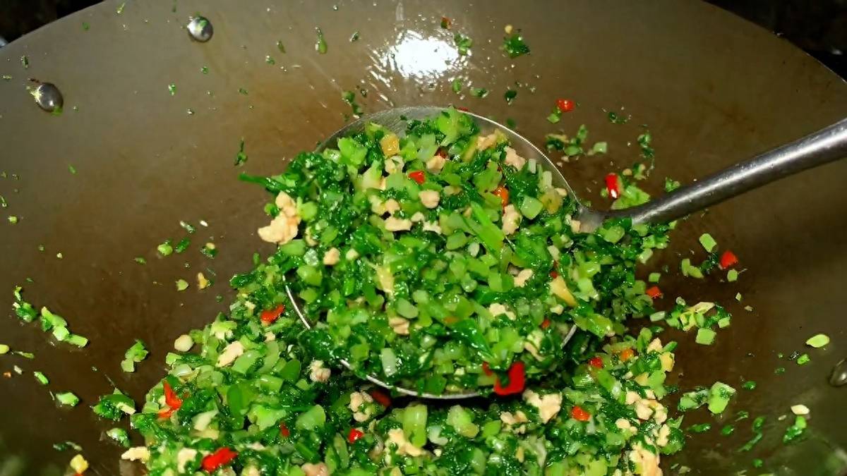 一位家庭主妇在明亮现代厨房中使用铁锅翻炒芹菜和圆椒,手握锅柄倾斜翻动食材,锅中蔬菜正在受热翻滚,蒸汽升腾,体现真实烹饪过程,背景可见调料瓶和砧板 家庭厨房中正在翻炒芹菜与圆椒的场景