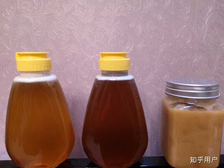 一张展示蜂蜜分别装在透明玻璃瓶、棕色玻璃瓶、陶瓷罐和塑料瓶中的对比图,背景为木质厨房台面,光线柔和,突出不同容器对蜂蜜色泽和质感的影响 蜂蜜在不同材质容器中的对比图