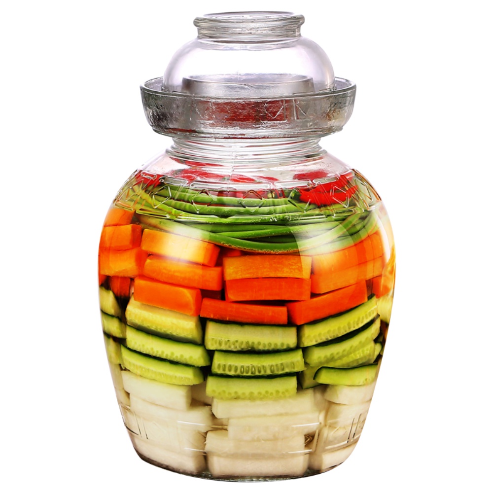一个透明玻璃腌制罐内清晰可见分层结构:底部为拍裂的大蒜和辣椒段,中间插有整株莳萝,四周紧密排列着深绿色小黄瓜,顶部覆盖一片完整的浅绿色葡萄叶 玻璃罐中分层装填香料与小黄瓜