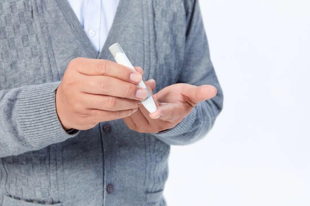 一位中年男性坐在餐桌前,正在用血糖仪测试指尖血液,桌上摆放着记录本、药物盒以及一份清淡饮食餐盘,其中包括清炒豆角、杂粮饭和蒸鱼,体现健康管理的生活方式 糖尿病患者使用血糖仪检测指尖血糖的场景