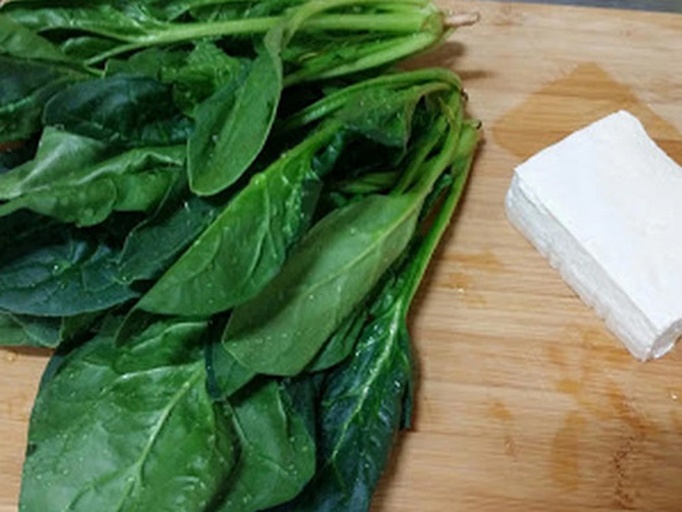 新鲜深绿色菠菜叶片与白色块状千叶豆腐并列摆放于木质砧板上,背景为厨房环境,光线柔和,突出食材自然质感 菠菜与千叶豆腐食材特写