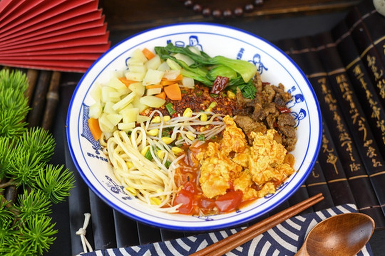 两碗面并列摆放,左侧是用西葫芦制成的螺旋状蔬菜面,清淡透明;右侧是传统的黄色小麦意大利面,背景为白色餐桌,突出两者在外观和质感上的差异 西葫芦面条与传统面条对比图