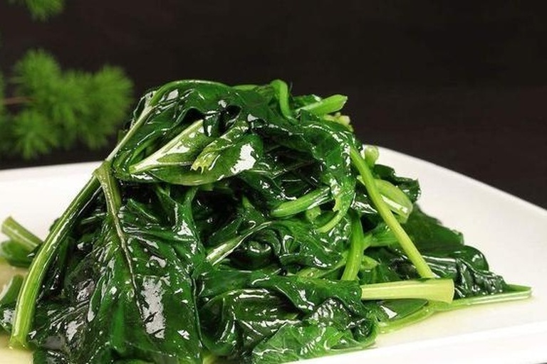 清炒大叶菠菜出锅特写：翠绿饱满的菠菜整齐铺于浅口青花瓷盘中，表面油润光亮，零星金黄蒜片点缀其间，热气微升