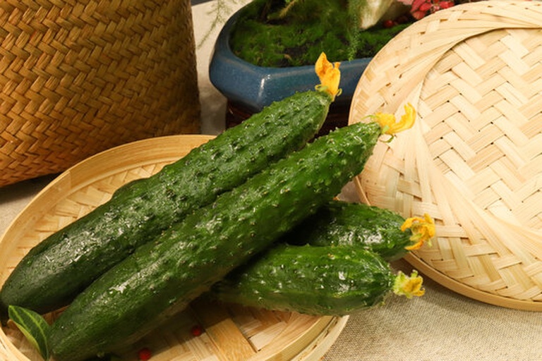 新鲜翠绿的小黄瓜整齐摆放在竹编菜篮中,旁边是一束刚采摘的白色带蕾韭菜花,背景为田园农家厨房环境,阳光透过窗户洒在台面上 清新食材组合