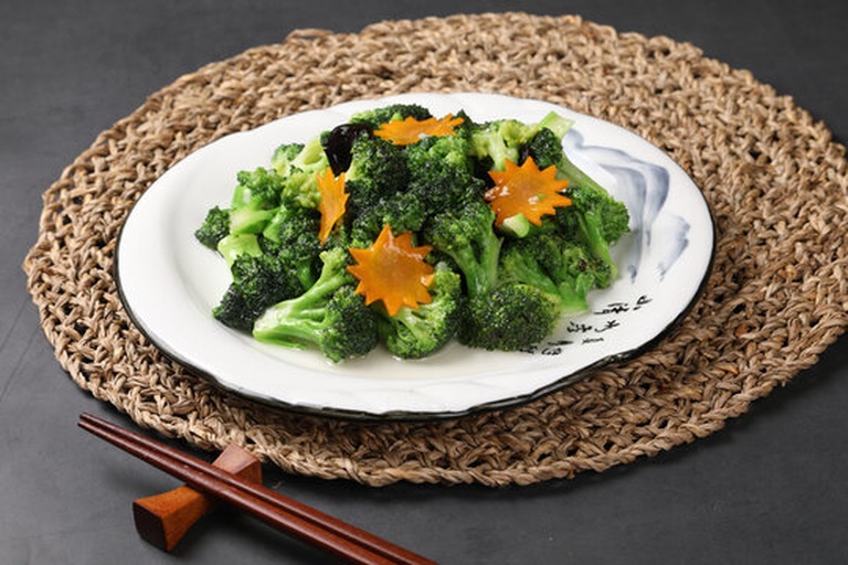 白色瓷盘中盛放清炒西兰花,花蕾青翠、茎部半透明,表面点缀金黄蒜末,旁边配有米饭和木质筷子,展示健康中式家常菜场景 家庭餐桌上摆盘精美的蒜蓉炒西兰花