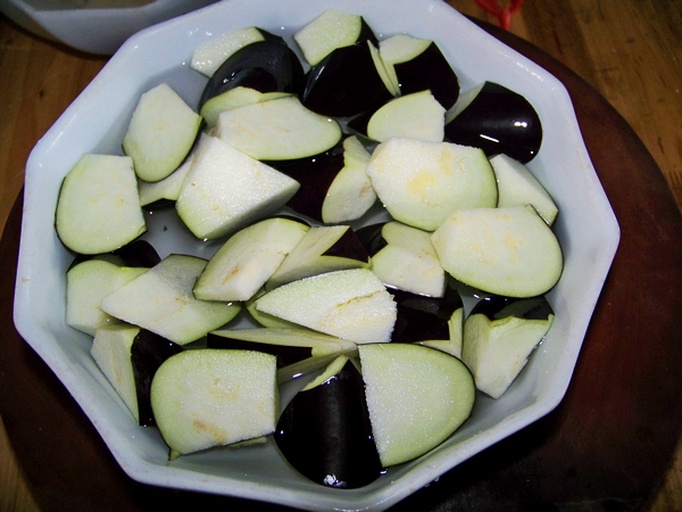 三格图片展示:第一格为切块茄子放入柠檬水中浸泡;第二格为用保鲜膜包裹生茄片放入冰箱冷藏;第三格为茄子块在沸水中焯烫,配有文字标注操作要点,背景为简洁厨房环境 防止茄子褐变的三种家庭处理方式示意图