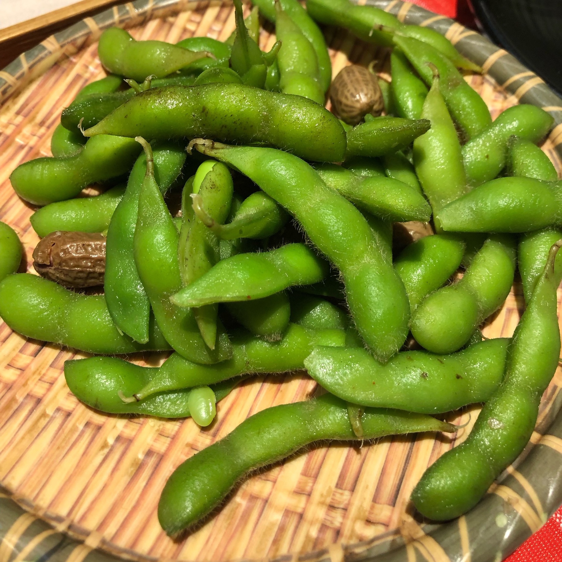 一盘新鲜翠绿的水煮毛豆,带壳整粒摆放于白色瓷盘中,背景虚化的餐桌上有竹筷和柠檬片点缀,展现健康轻食风格 毛豆特写