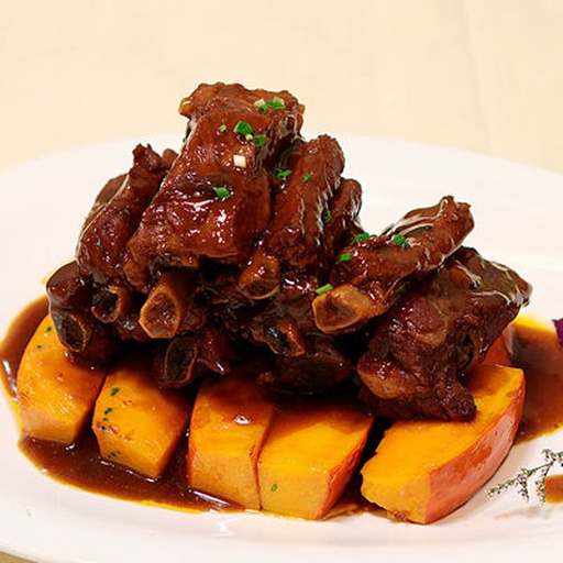 一盘刚出锅的贝贝南瓜炖排骨，排骨色泽红亮，南瓜金黄诱人，撒有葱花点缀，盛放在白色瓷盘中