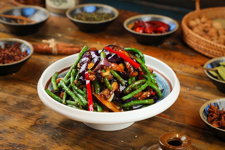 厨师正在用铲子在炒锅中翻炒线茄子和豆角，锅中食材翻滚，香气四溢
