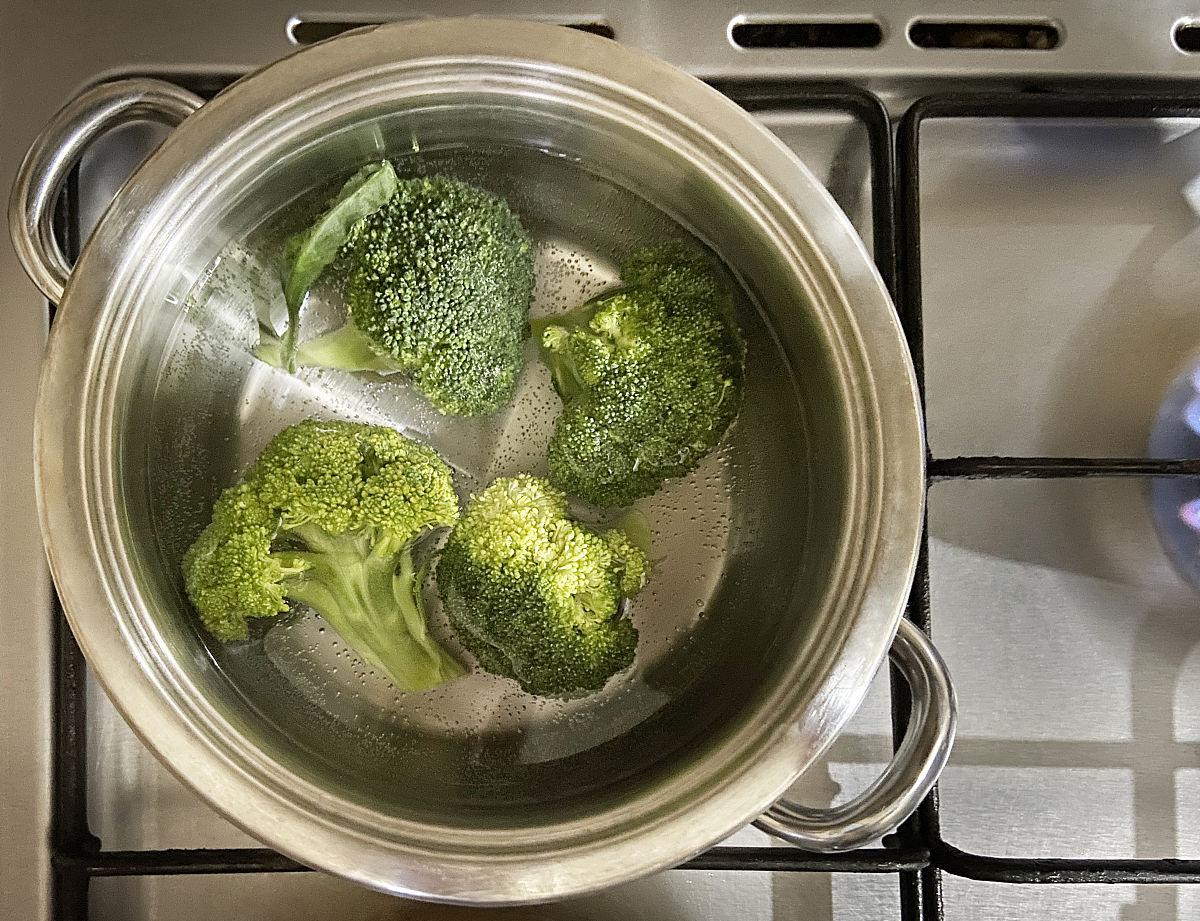 一位家庭主妇在厨房中用不锈钢锅清蒸西兰花,旁边配有切好的蒜末和橄榄油,灶台整洁,光线明亮,体现健康饮食的生活方式 家庭烹饪场景