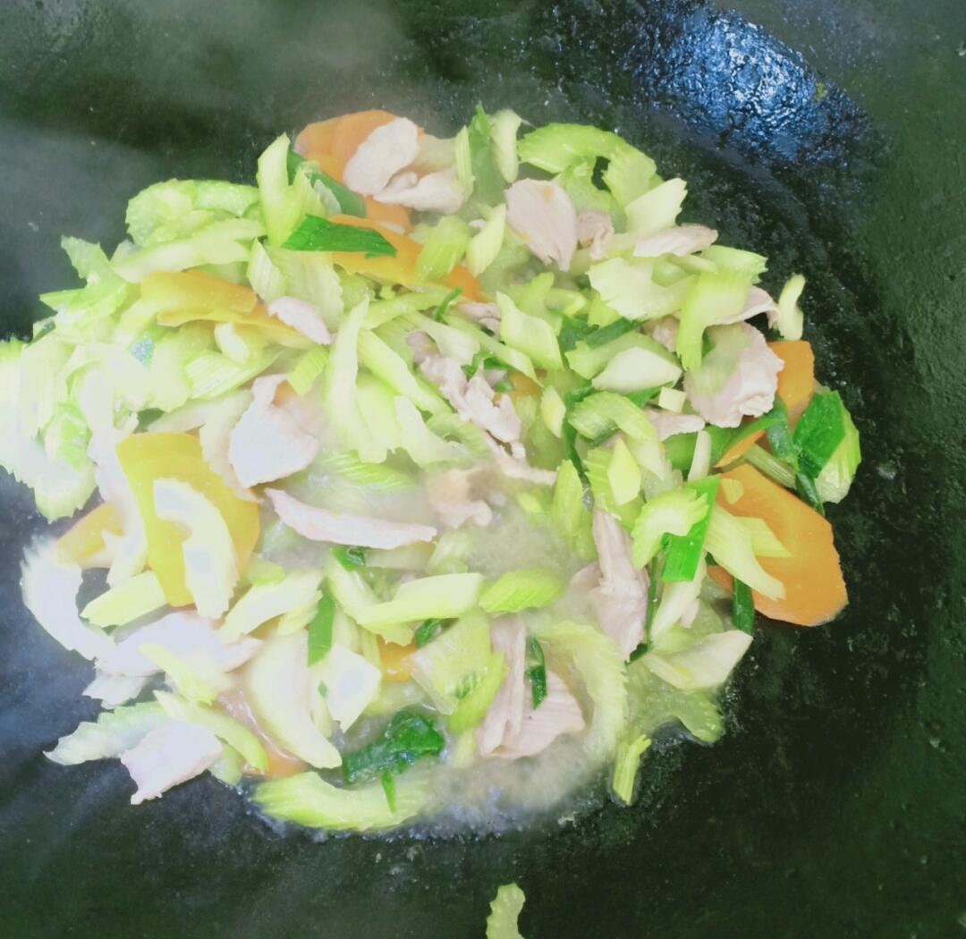 一位家庭主妇在厨房灶台前使用铁锅翻炒藕片与芹菜,动作自然,锅中热气腾腾,体现真实生活化烹饪情境 家庭厨房中正在翻炒藕和芹菜的过程抓拍