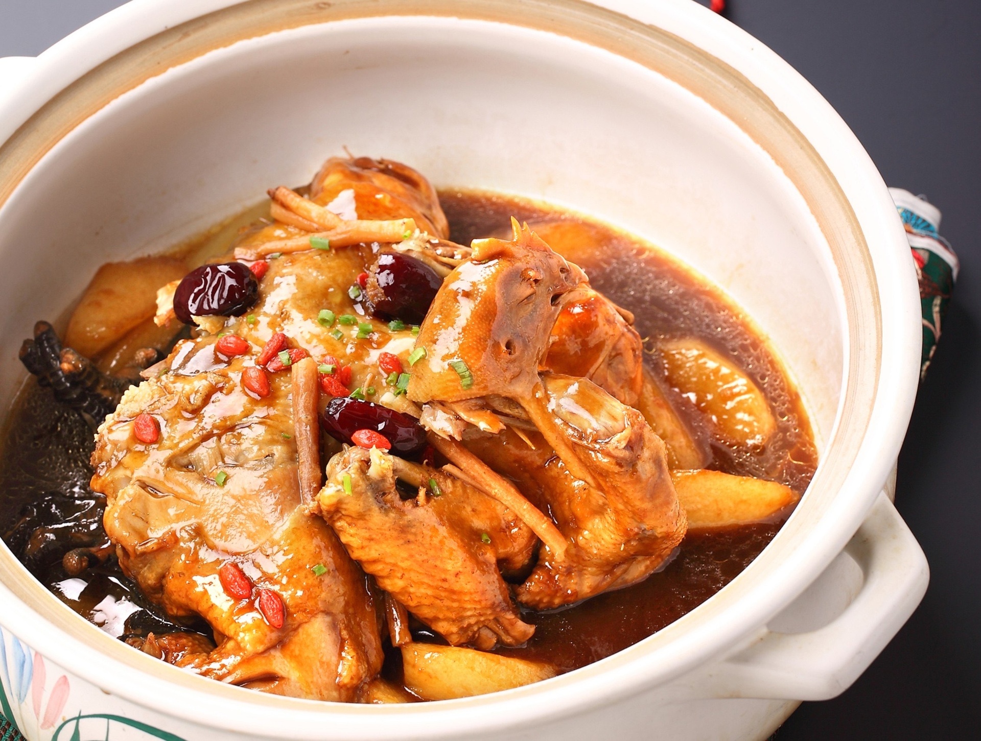 一口砂锅中正在炖煮油栗鸡块,汤汁微沸,油栗已剥壳呈金黄色,鸡肉块与枸杞、姜片同煮,营造出温补养生的视觉效果 油栗烹饪场景