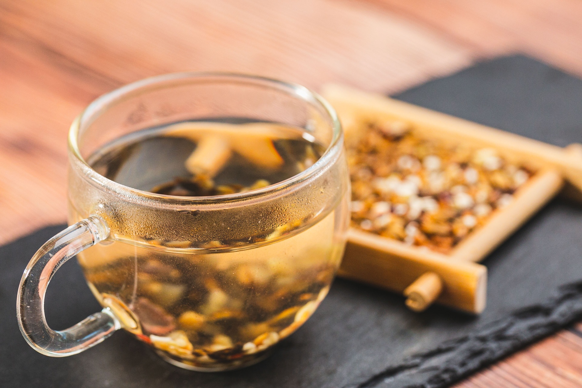 透明玻璃杯中正在冲泡奶油草莓茶,可见粉色草莓干与绿色茶叶交织,热水注入后色泽渐变为淡玫瑰色,旁边摆放干燥草莓片与茶罐,桌面木质纹理清晰,营造温馨养生氛围 奶油草莓茶冲泡过程展示