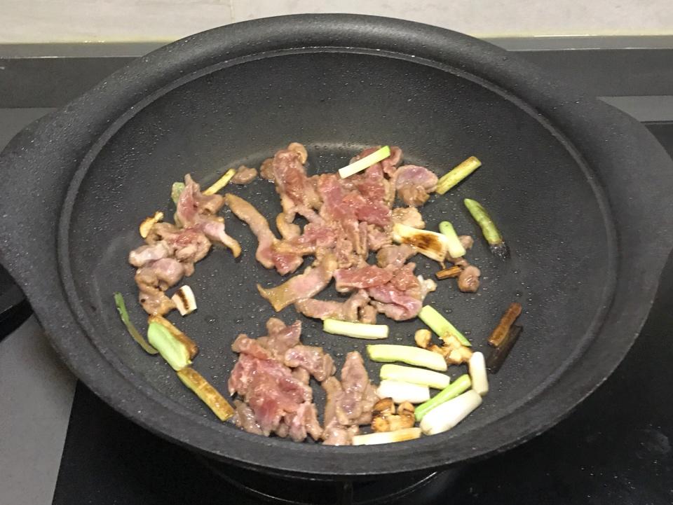 锅中鸡腿正在煎制,旁边是翻炒的大葱段,锅中飘出香气 煎制孜然鸡腿过程图