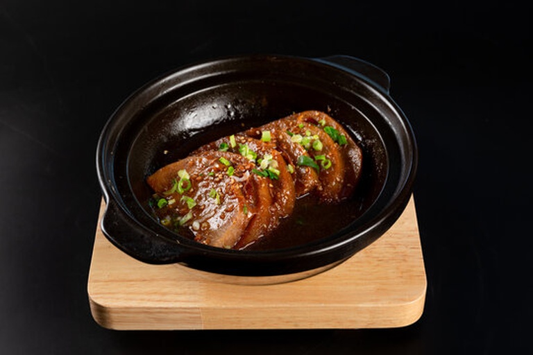 砂锅中正在炖煮的红烧肉,汤汁微沸,一块完整的八角漂浮在表面,旁边是色泽红亮的五花肉块,背景为木质灶台 红烧肉炖煮过程中八角清晰可见