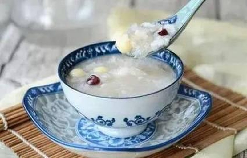 砂锅中小火慢煮的红枣桂圆莲子粥,表面泛着油光,旁边摆放去核灰枣、干龙眼肉、白色莲子和黄小米,展示食材准备全过程,适合家庭厨房场景 红枣桂圆莲子粥制作过程