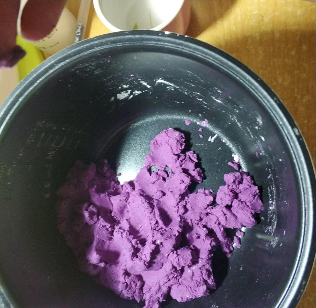 一名厨师正在将蒸熟的紫薯泥加入面团中,面团部分呈现淡紫色与绿色交织的效果,旁边摆放着新鲜紫薯块和搅拌工具,体现食材加工过程 厨房场景下紫薯用于制作健康甜品的过程