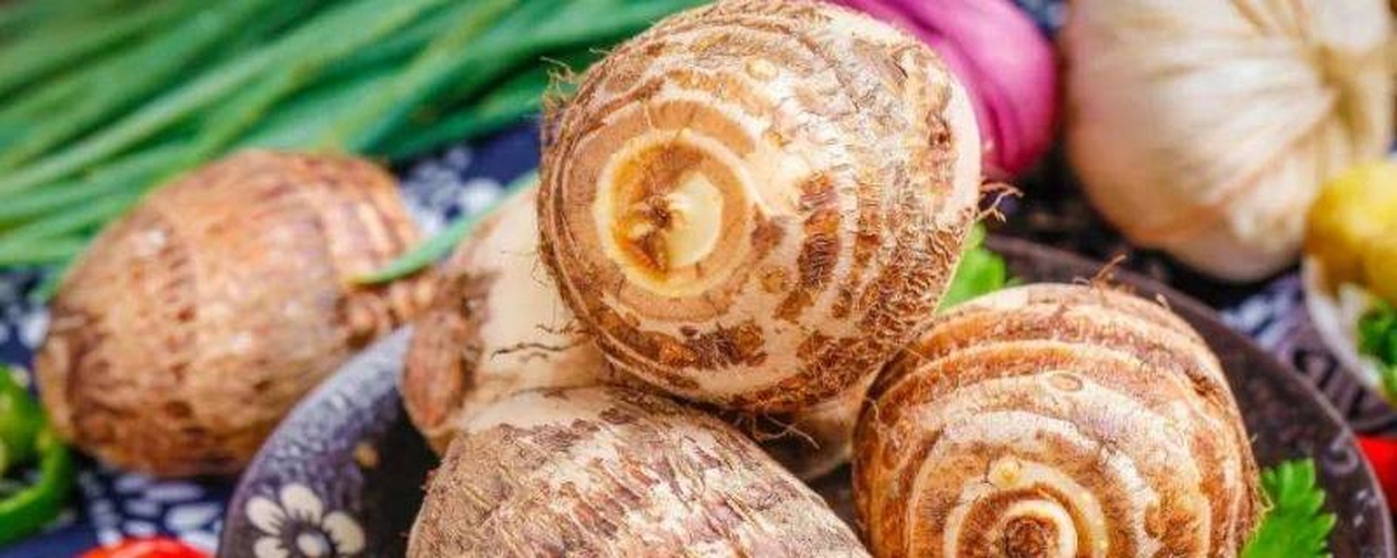 白色瓷盘中盛放着去皮后切成两半的小芋头,表面泛着油亮光泽,撒有翠绿葱花和少许红椒丝,背景虚化的竹筷暗示即将享用,展现江南家常菜的精致与质朴 江南风味家常菜:葱油芋艿特写