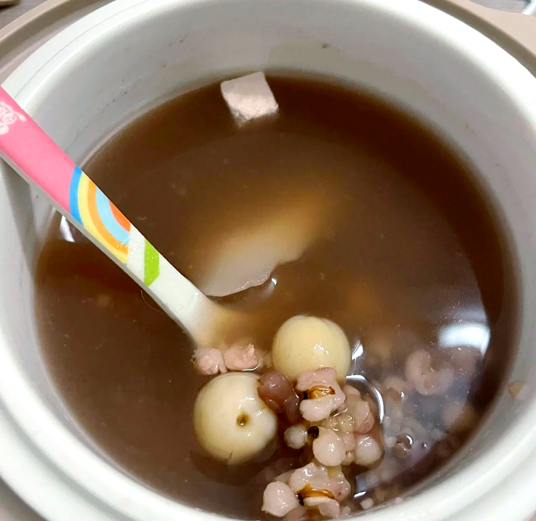 一碗热气腾腾的莲子汤，汤色呈淡红色，碗中漂浮着几颗去芯莲子
