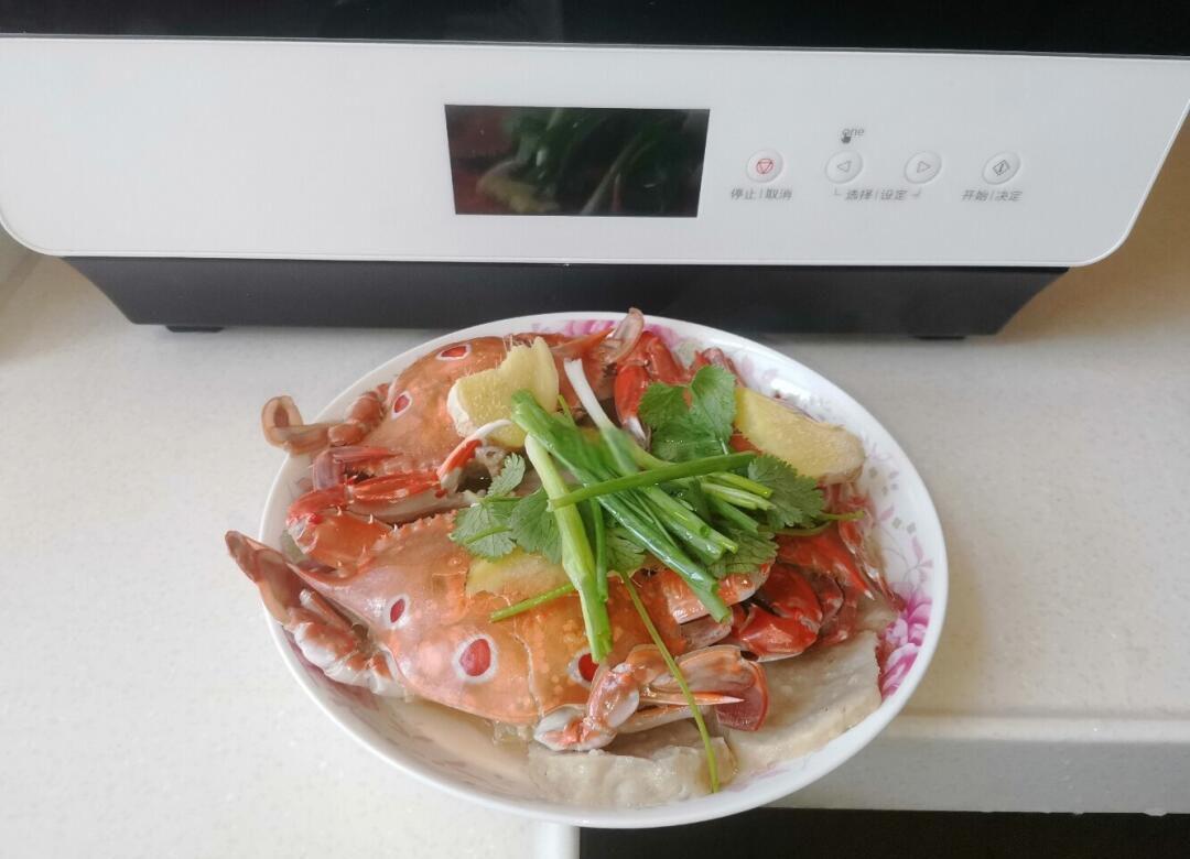 一位家庭主妇在厨房操作台前,将冷藏后的熟大闸蟹放入蒸锅,旁边摆有生姜片和醋碟,墙上挂钟显示时间为中午12:15,窗外阳光明媚,体现日常家庭健康饮食场景 家庭厨房中安全食用大闸蟹场景图