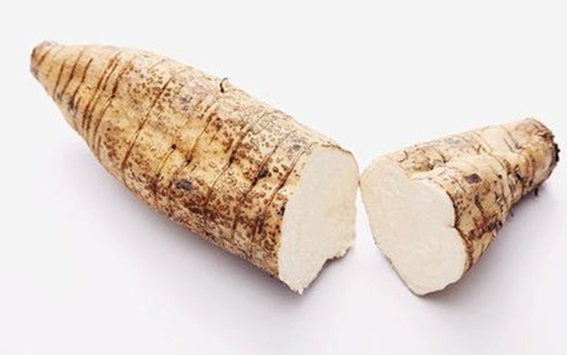 一根新鲜山药被横向切开,露出内部组织,其中一侧出现明显的淡紫色斑块,其余部分为乳白色,表面湿润有光泽,背景为木质砧板 山药切面呈现淡紫色区域特写