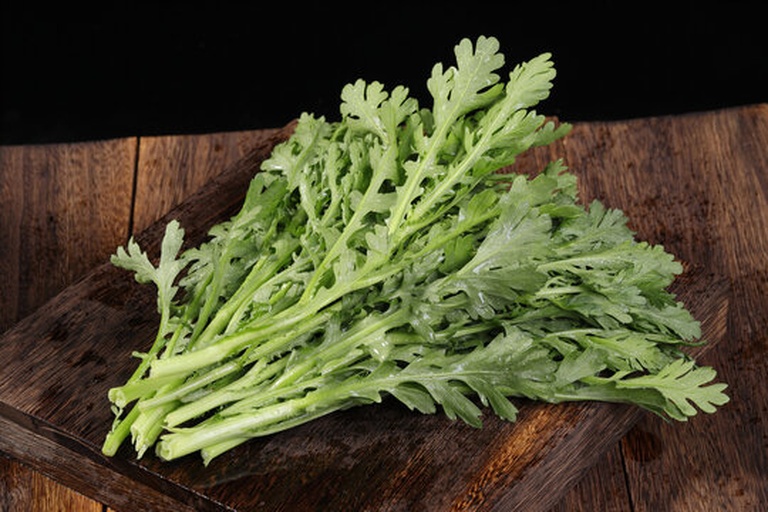 一束新鲜翠绿的蒿子杆,茎部洁白,叶片饱满,整齐摆放在木质砧板上,背景为厨房操作台,光线柔和自然 新鲜蒿子杆特写