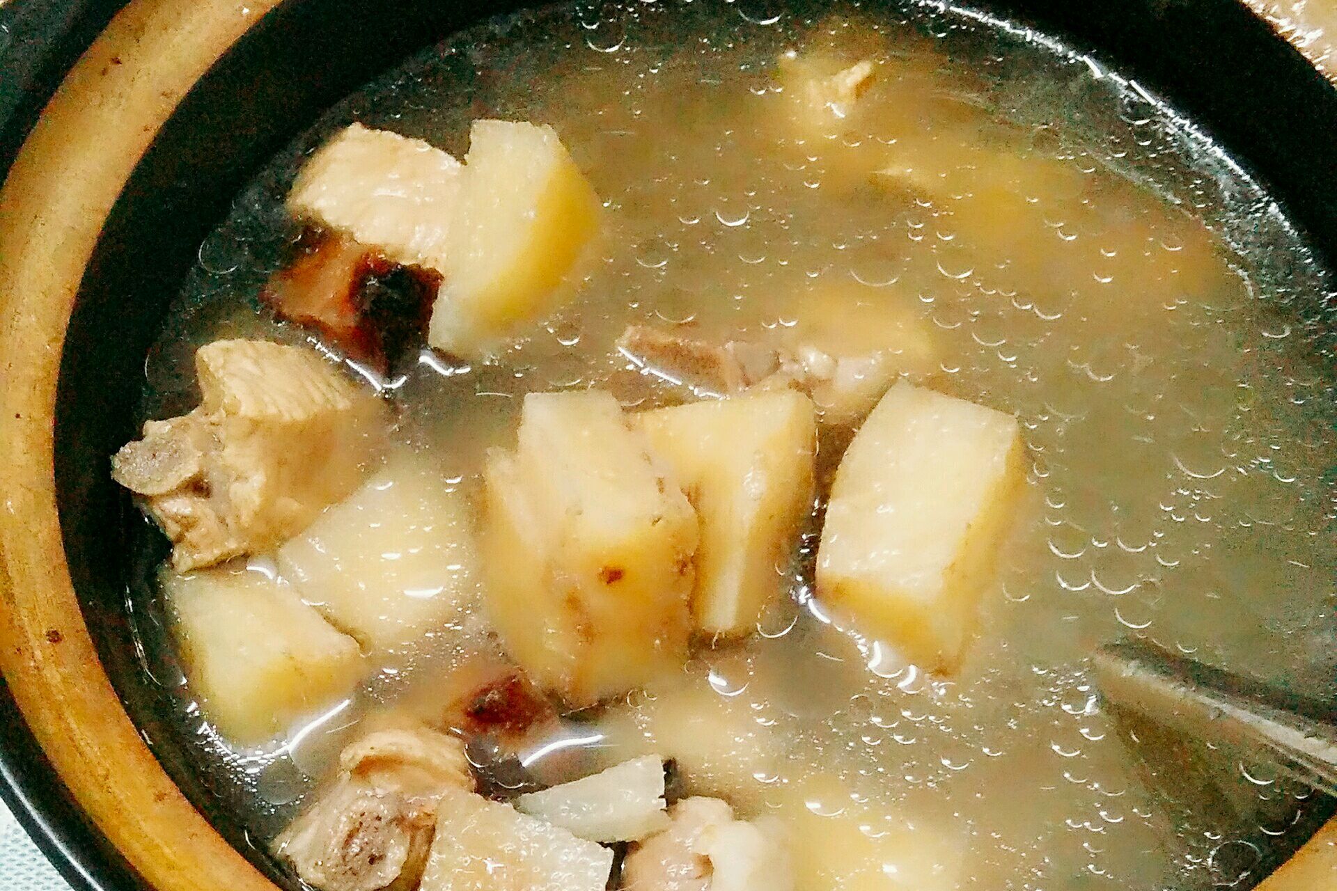 深色砂锅中正在炖煮胡萝卜土豆炖鸡腿肉,汤汁呈红褐色,鸡块与蔬菜混合翻滚,表面浮着油亮光泽,锅边配有姜片、葱段、八角等香料,热气升腾 炖煮过程图