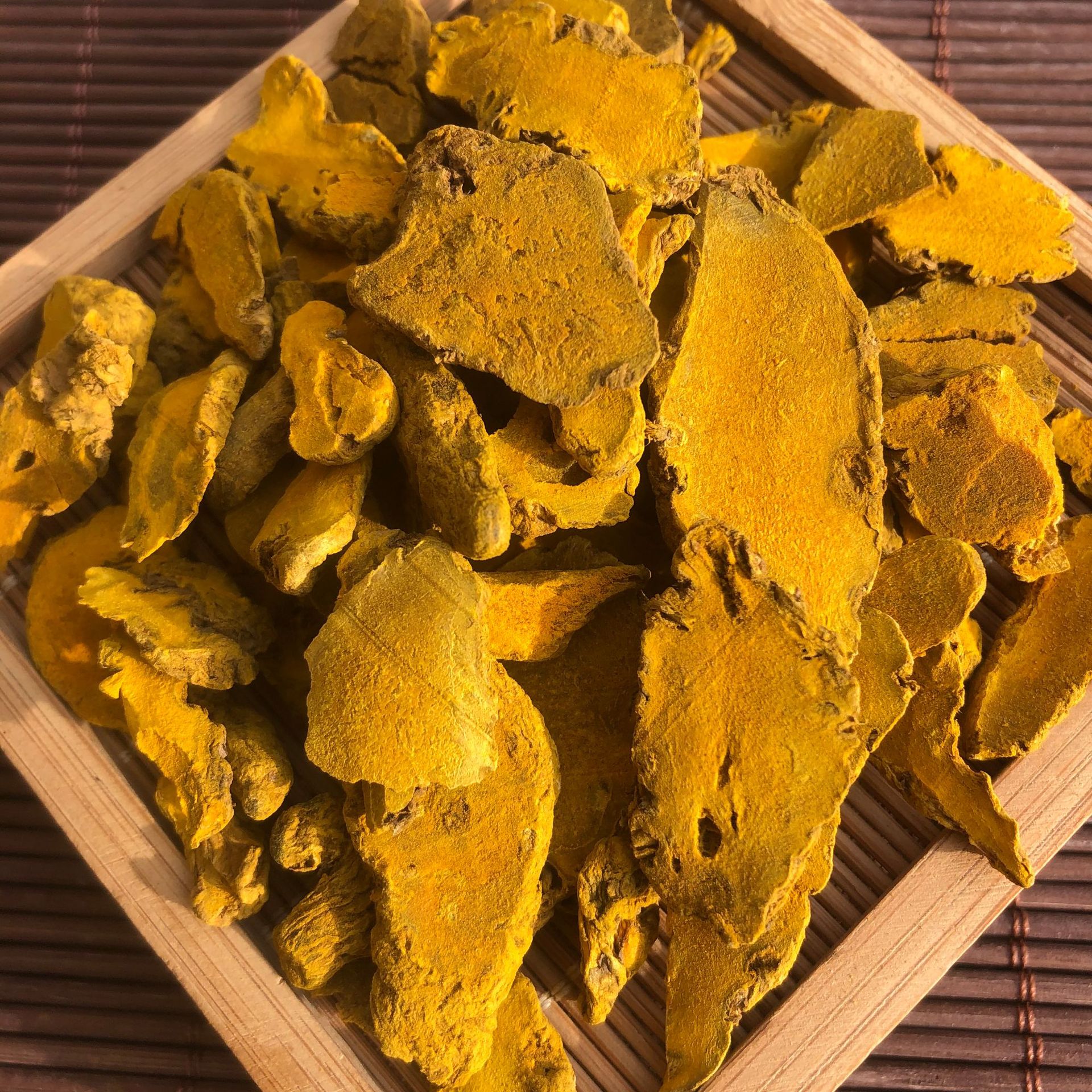 一张整洁的白色桌面上陈列多种黄姜相关产品:棕色玻璃瓶装姜精油、铝塑板包装的黄姜胶囊、纸袋装原味姜茶、研磨成粉的黄姜粉罐子,以及一小碟切片晒干的黄姜药材。背景虚化,突出产品的多样性和现代化包装设计 黄姜保健品与日常制品陈列图