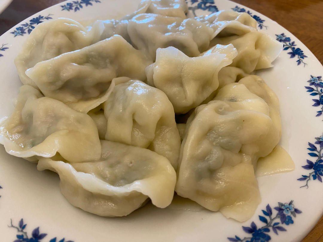 一盘热气腾腾的大葱猪肉馅饺子,饺子皮透明,肉馅隐约可见,摆放在木质托盘中,背景为中式厨房 大葱猪肉馅饺子成品图