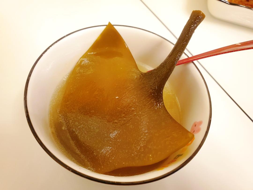 一锅正在熬煮的深褐色海带汤,海带上浮着细小泡沫,背景为传统日式厨房环境,灶台上有陶制汤锅和木勺,突出海带释放鲜味的过程 海带熬煮过程示意图