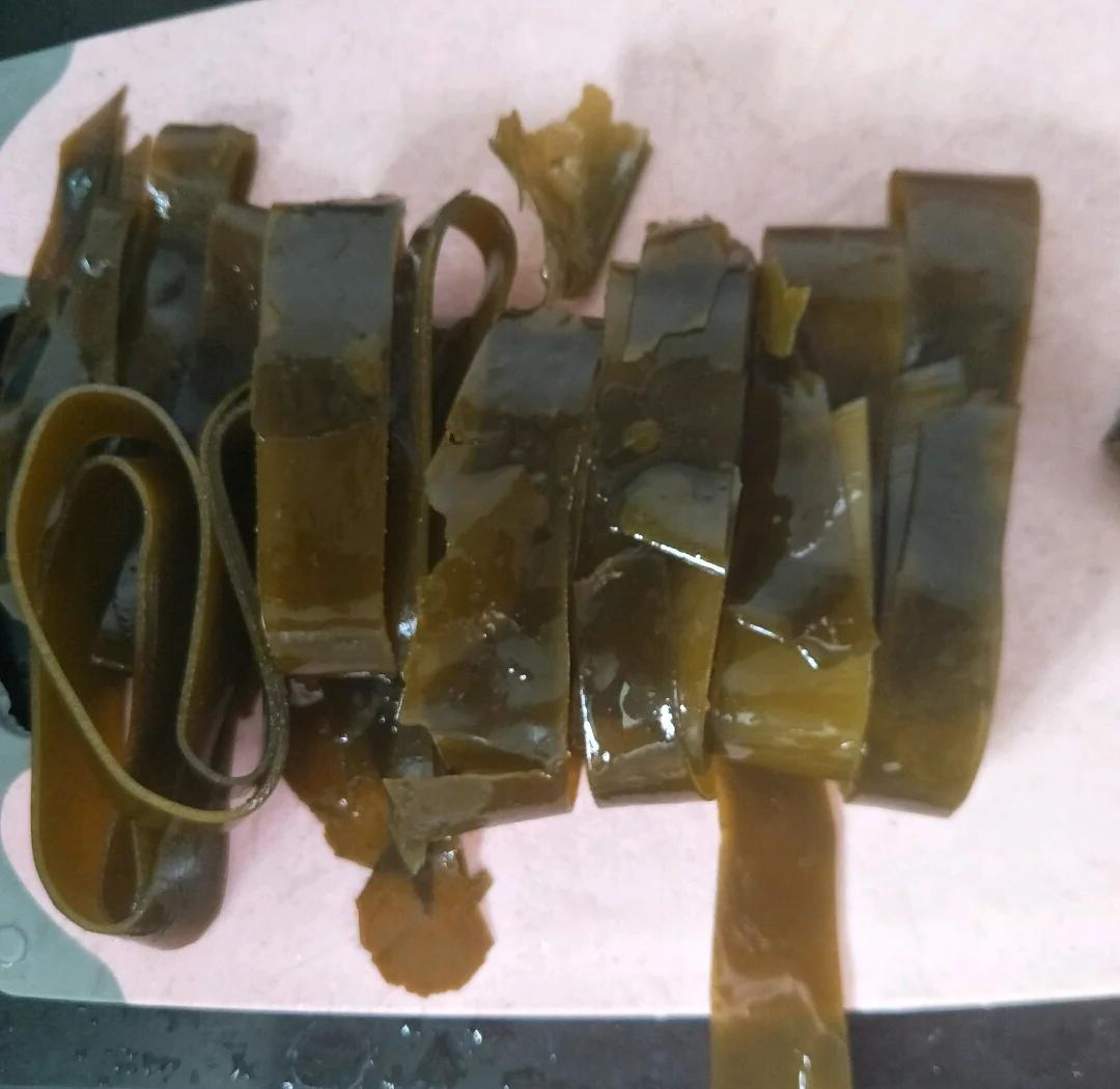 新鲜干海带平铺于木质砧板,刀锋沿深褐色纵向叶脉纹理精准剪切成菱形小段,边缘整齐无毛刺,背景可见滤网与流动清水 干海带顺叶脉剪段特写