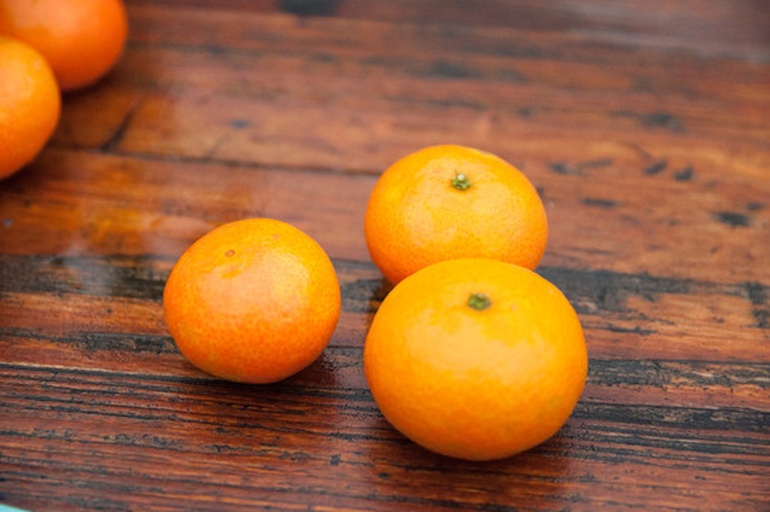 一颗成熟的蜜橘静置于木质桌面上,果皮呈亮橙黄色,表面光滑有光泽,底部清晰可见一个圆形微凹的‘肚脐’结构,周围无损伤或斑点,背景为柔和的自然光,营造出温暖清新的氛围 蜜橘整体特写