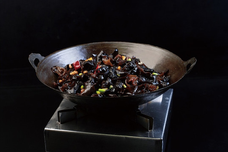 一位厨师在家庭厨房中用铁锅翻炒莲藕片、胡萝卜丁和黑木耳,锅中热气腾腾,食材色彩分明,旁边案板上摆放着待切的青椒和玉米粒,展现真实烹饪过程 厨房中正在翻炒莲藕与配菜的场景