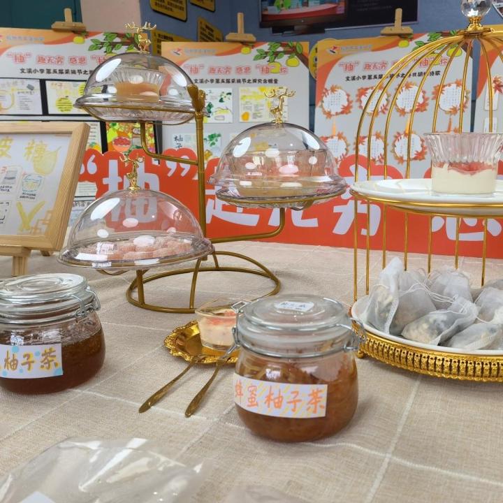 一张白色瓷盘中摆放着三种以柚子为主的创意美食:左侧是粉红色柚子果粒拌入芝麻菜的沙拉,中间是一杯透明玻璃杯装的金黄色蜂蜜柚子茶,右侧是用柚子皮制成的晶莹剔透的蜜饯,整体布置清新自然,适合春季主题 柚子创意料理拼盘