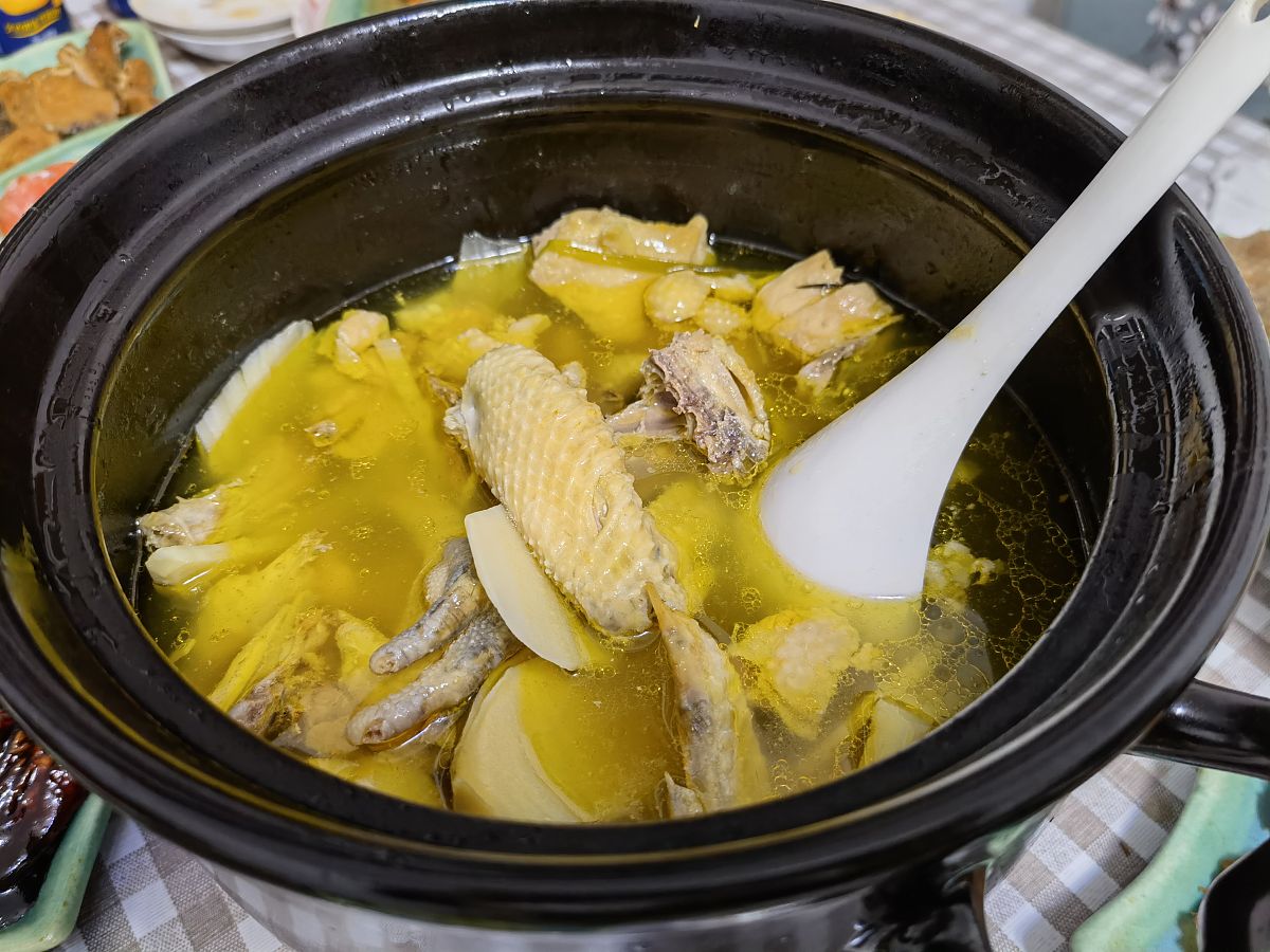 砂锅中小火慢炖的咸鸡腿，汤汁微沸，大葱段清晰可见