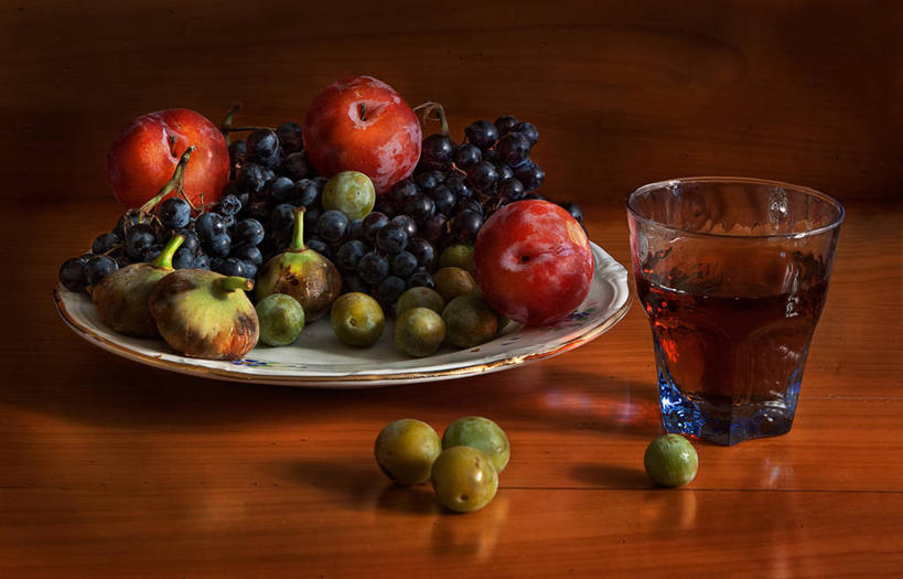 一瓶琥珀色的李子酒置于木质桌面上,酒液透亮,可见瓶底沉淀的李子残渣,周围摆放玻璃酒杯和几颗新鲜青李,光线柔和,突出自然健康氛围 李子酒成品色泽展示