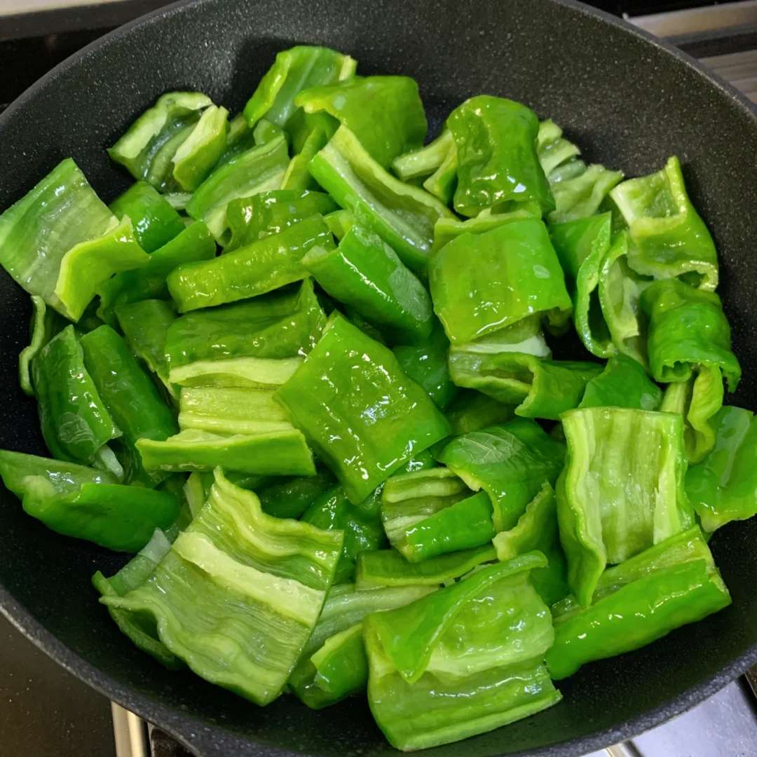 一位厨师正在厨房操作台上分别切分线椒和杭椒,左侧砧板上是已切段的深绿色线椒,右侧是切成圈的翠绿杭椒。背景可见炉灶上正在翻炒的菜肴,锅中食材冒起青烟,营造出真实的中式烹饪氛围 厨房中使用线椒与杭椒烹饪的场景