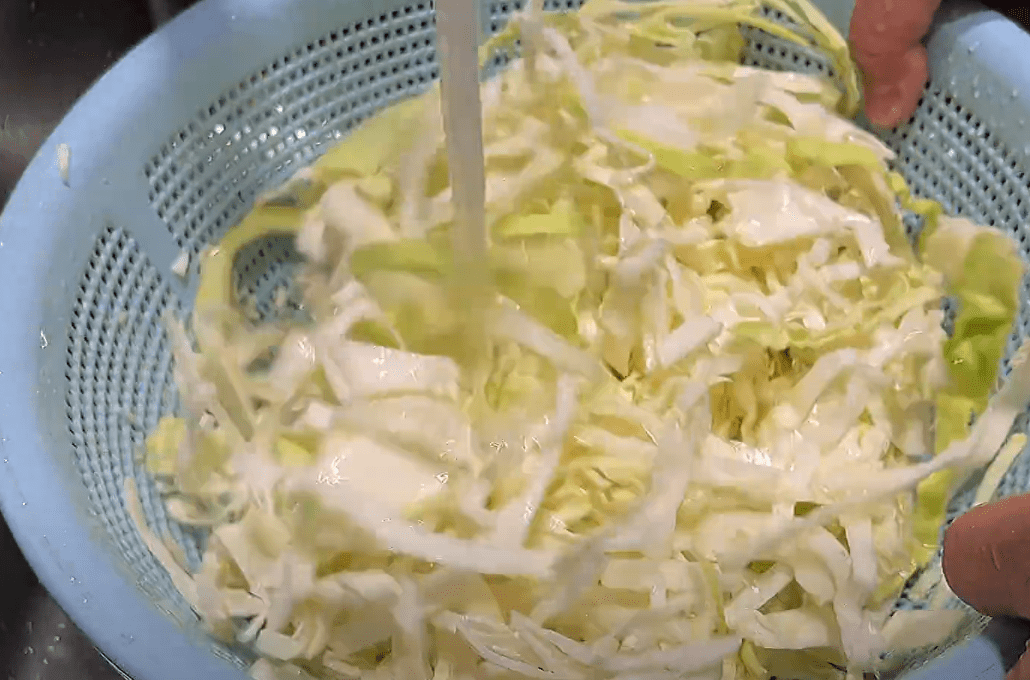 一名厨师正在厨房操作台上对紫红色茎秆的红菜心进行清洗,随后用刀将其斜切成段,旁边摆放着削皮刀和沥水篮,背景为整洁的厨房环境 红菜心清洗与切段过程