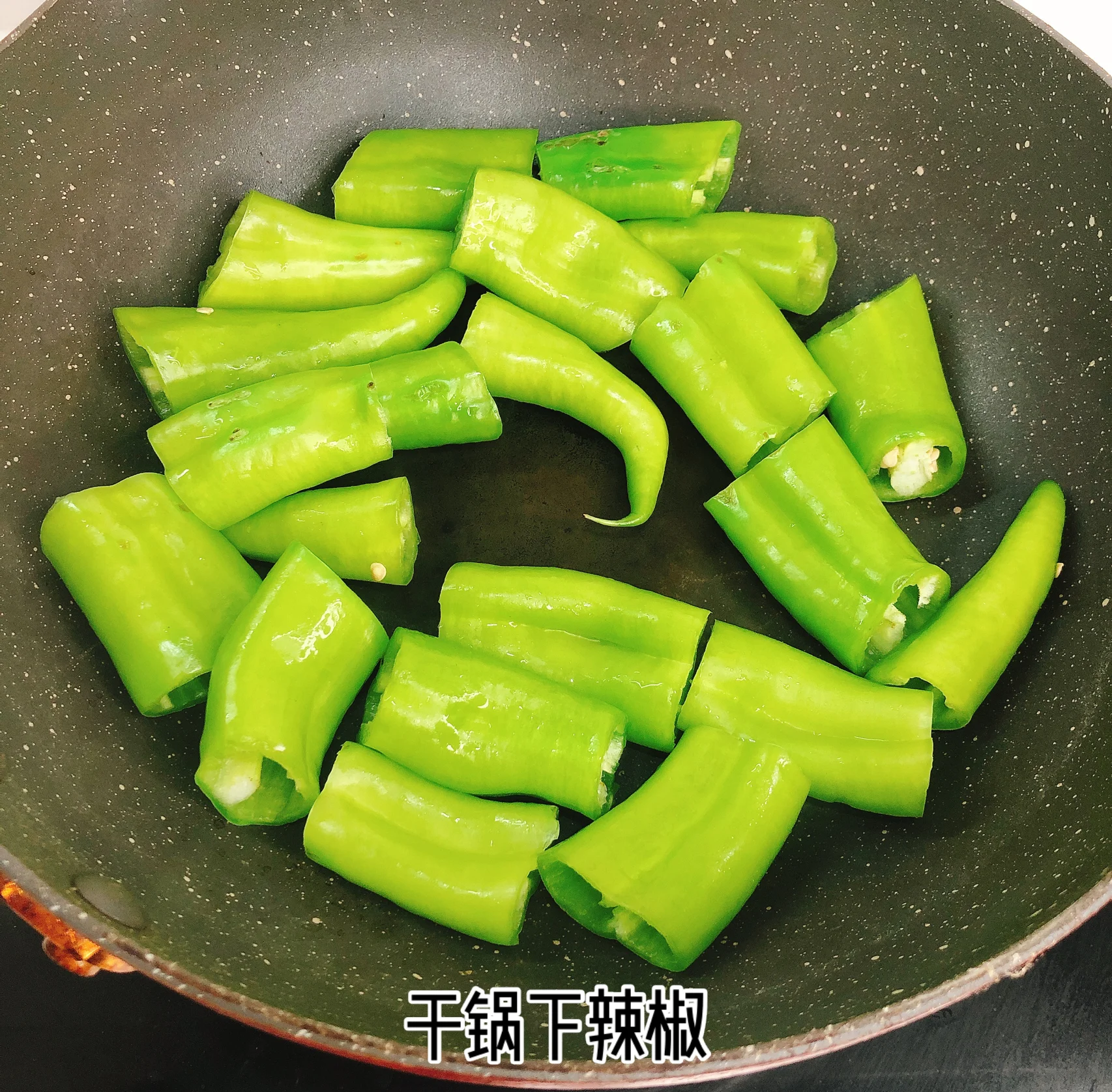 烧椒过程特写：青椒在干锅中受热起虎皮泡，表皮呈深褐与墨绿交织斑块，椒体微微弯曲，锅底无油渍，灶火呈中高蓝焰