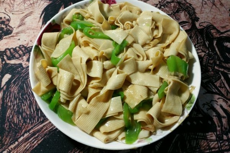 尖椒豆皮出锅特写：铁锅中菜肴油亮诱人，青翠尖椒丝与米黄豆皮条交错分明，豆皮表面微卷泛琥珀光泽，锅底无多余汤汁，可见细密油星与零星蒜末点缀